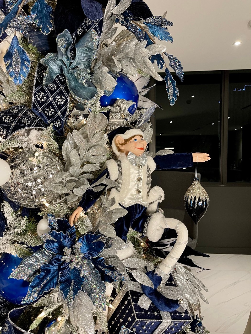 An elf, mid-reach, holding an ornament that has not been hung yet.
