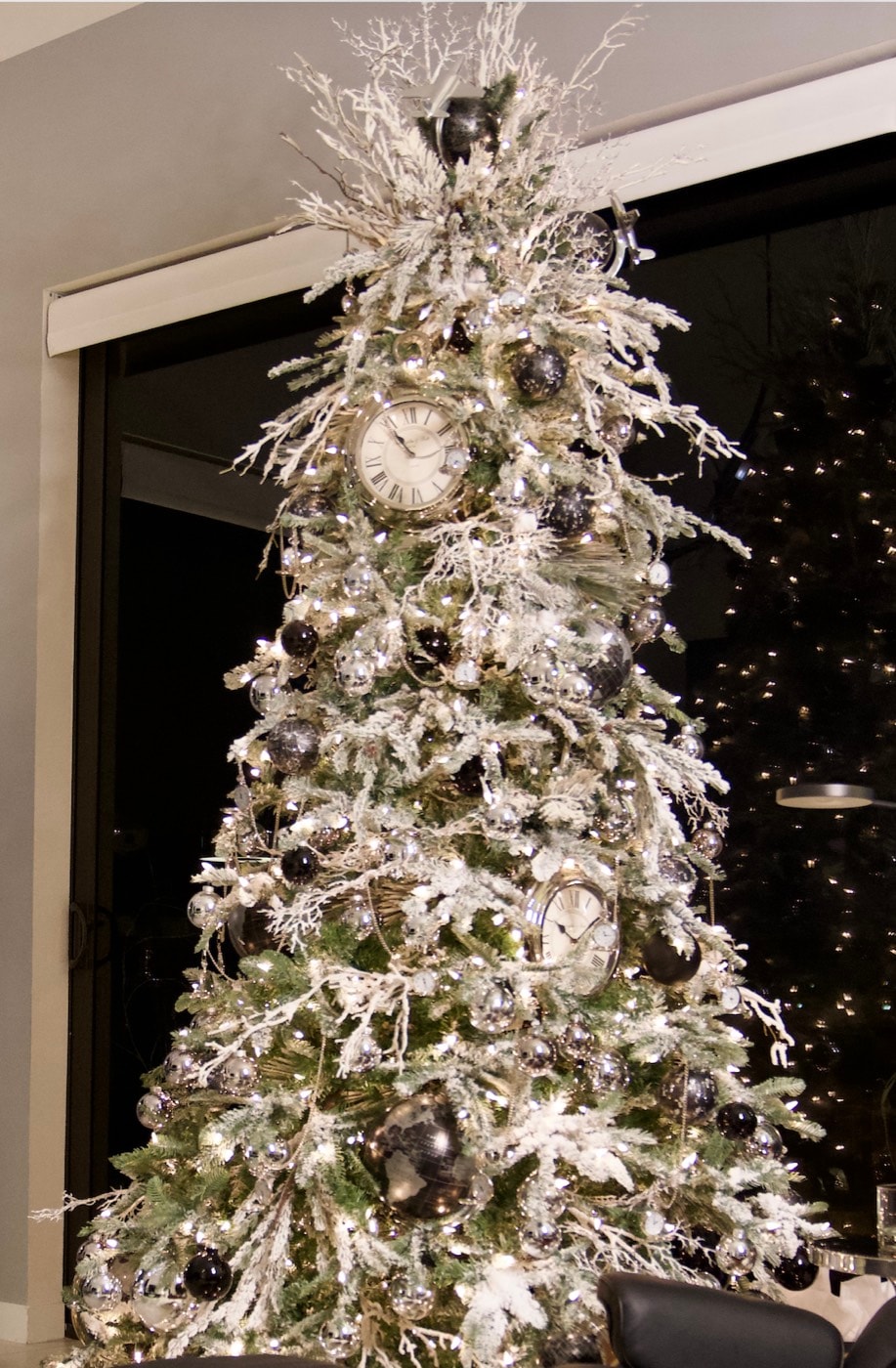 Clock faces among flocked branches, black baubles between them.